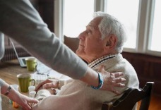 A caregiver gently supporting an elderly man at his kitchen table